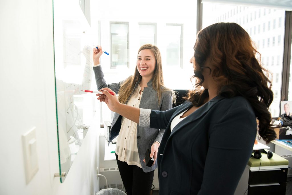 Zwei Personen arbeiten gemeinsam an einem Whiteboard im Büro.